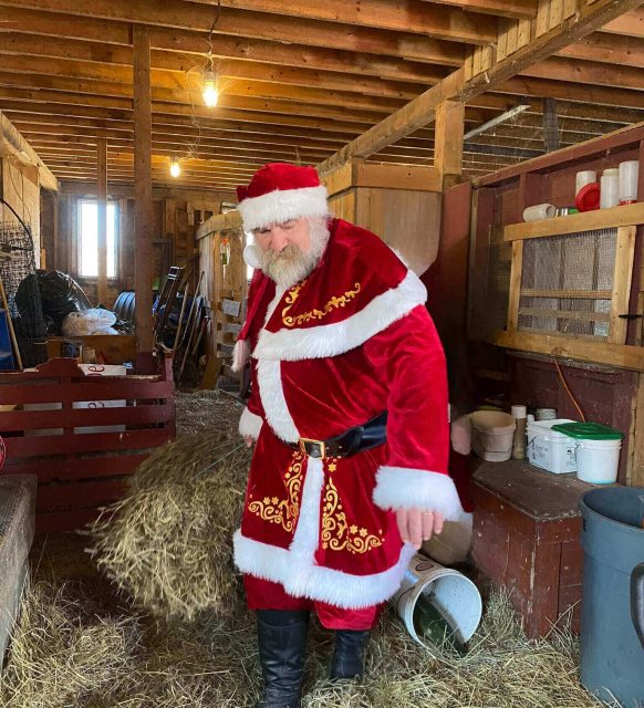 Santa Claus in a barn holding a metal bucket.