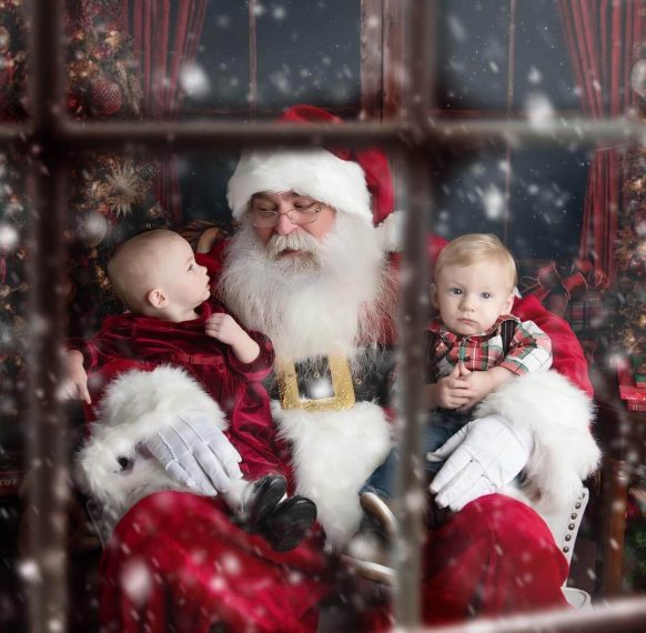 Santa Claus holding two babies in a festive, snowy setting.