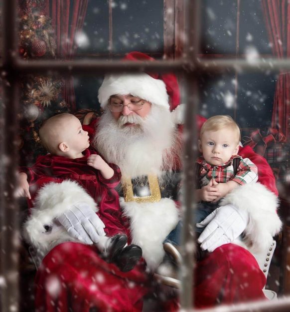 Santa Claus holding two babies in a festive, snowy setting.